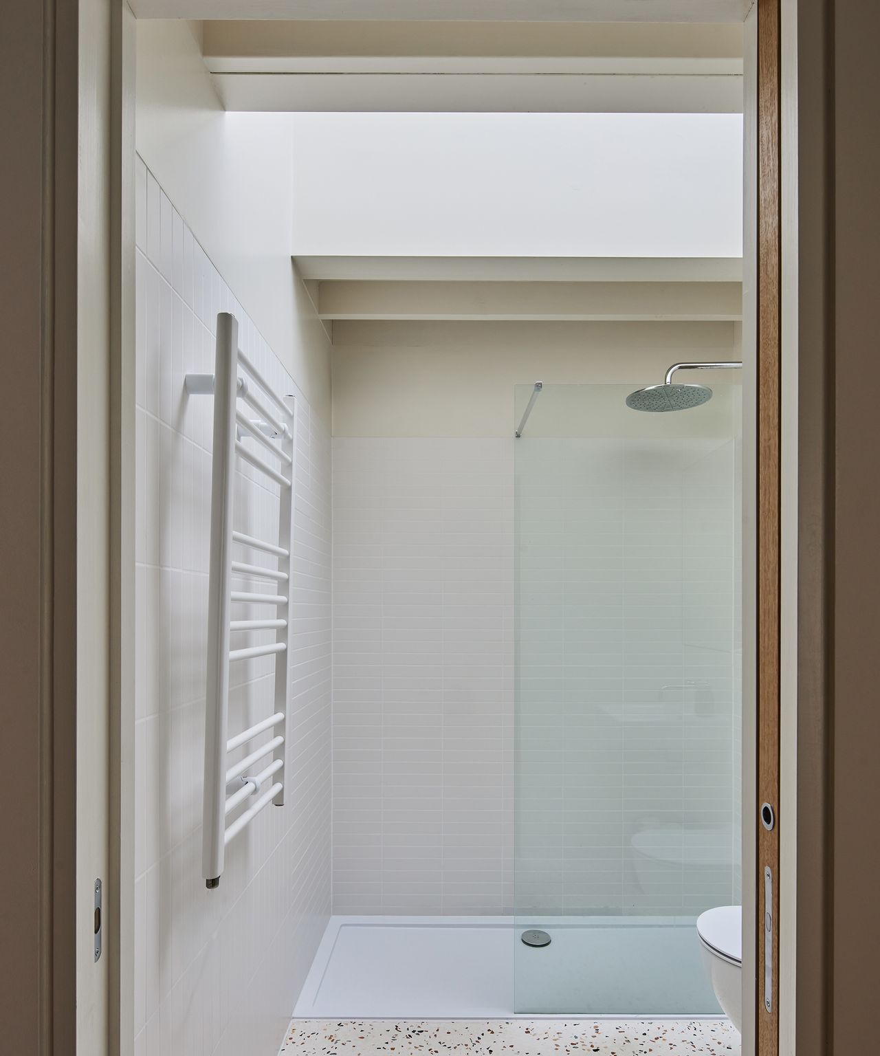 A small bathroom with terrazzo floor tiles and walk-in shower and ceiling light to allow plenty of natural light in