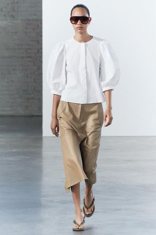 a model wears a white poplin blouse with beige capri pants