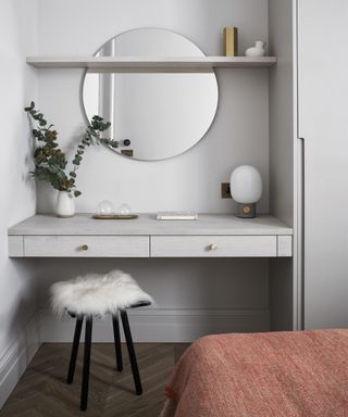 A bedroom with built-in dressing table, circular mirror and fluffy seat