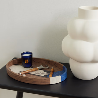 A wooden tray with a bottle opener and candle inside, next to a white sculptural vase.