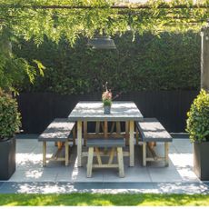 Outdoor seating area with cushions beneath wooden pergola with festoon lights and hanging pendant light