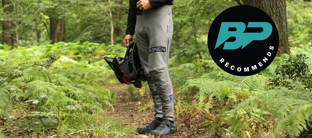 A model wearing the Renen MTB Pant on a trail lined by ferns and a BikePerfect recommends logo