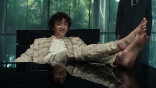 Boy Kavalier smiling with his shoe-less feet resting on a table in Alien: Earth