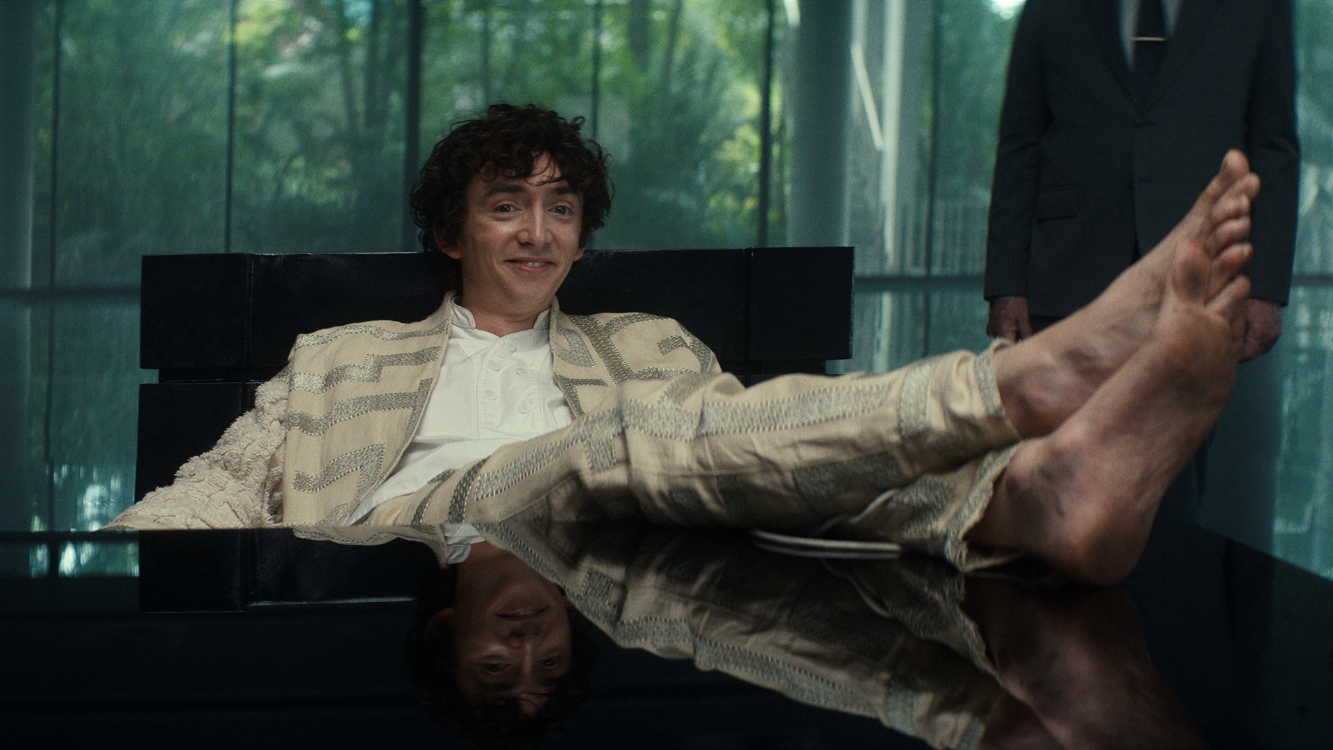 Boy Kavalier smiling with his shoe-less feet resting on a table in Alien: Earth