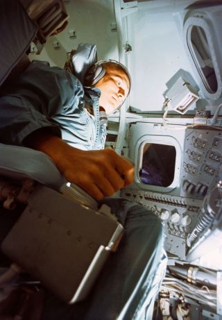 a man in a flight suit holds a flight stick in small cockpit