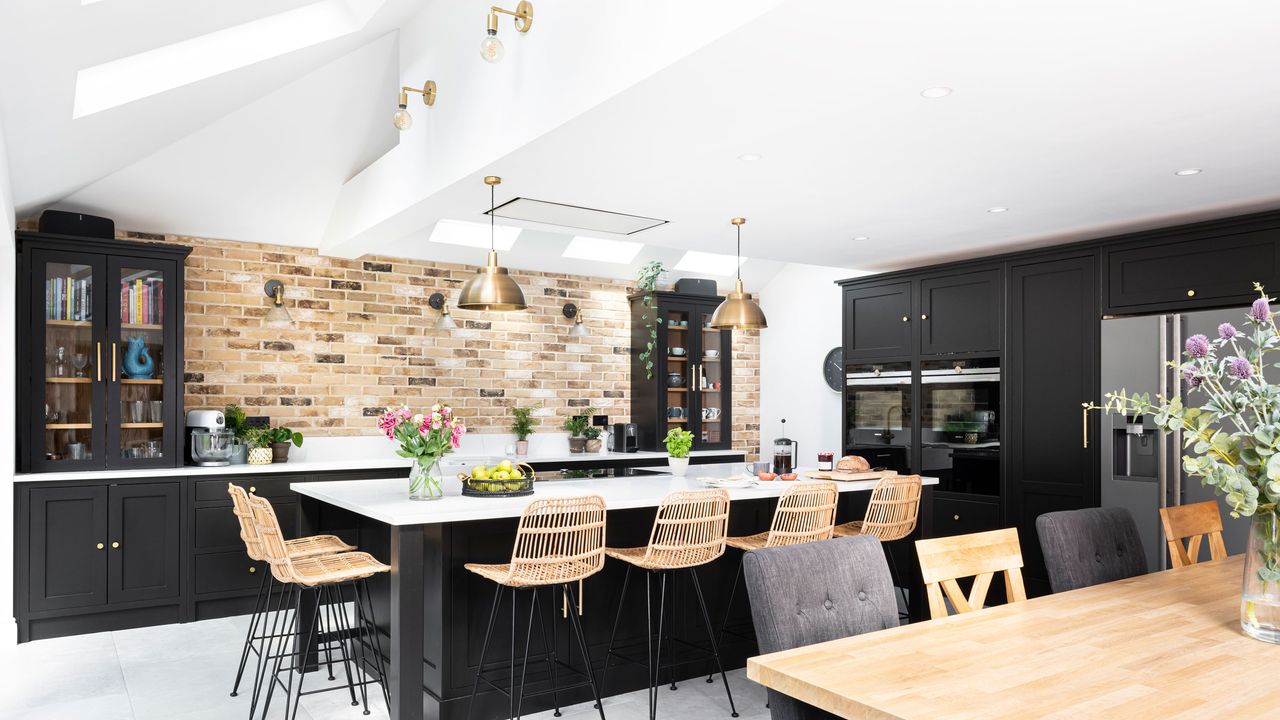 Black kitchen cabinets with a kitchen island with a white ceiling and brass light fittings