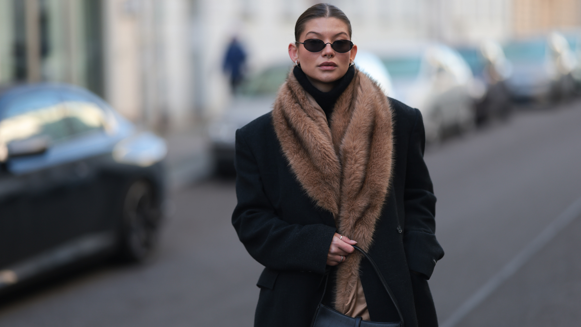 Woman with sleek centre parted hair, faux fur scarf and black trench with sunglasses