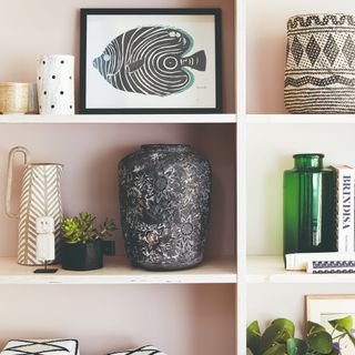 Pink bookshelves displaying curated decor including a fish print in a black frame