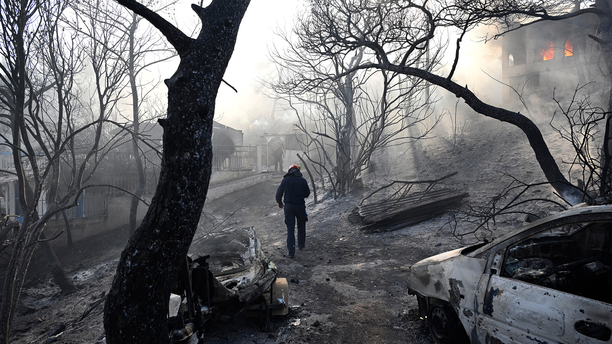 A firefighter walks through an ash-covered area during a wildfire on the island of Salamina, Greece
