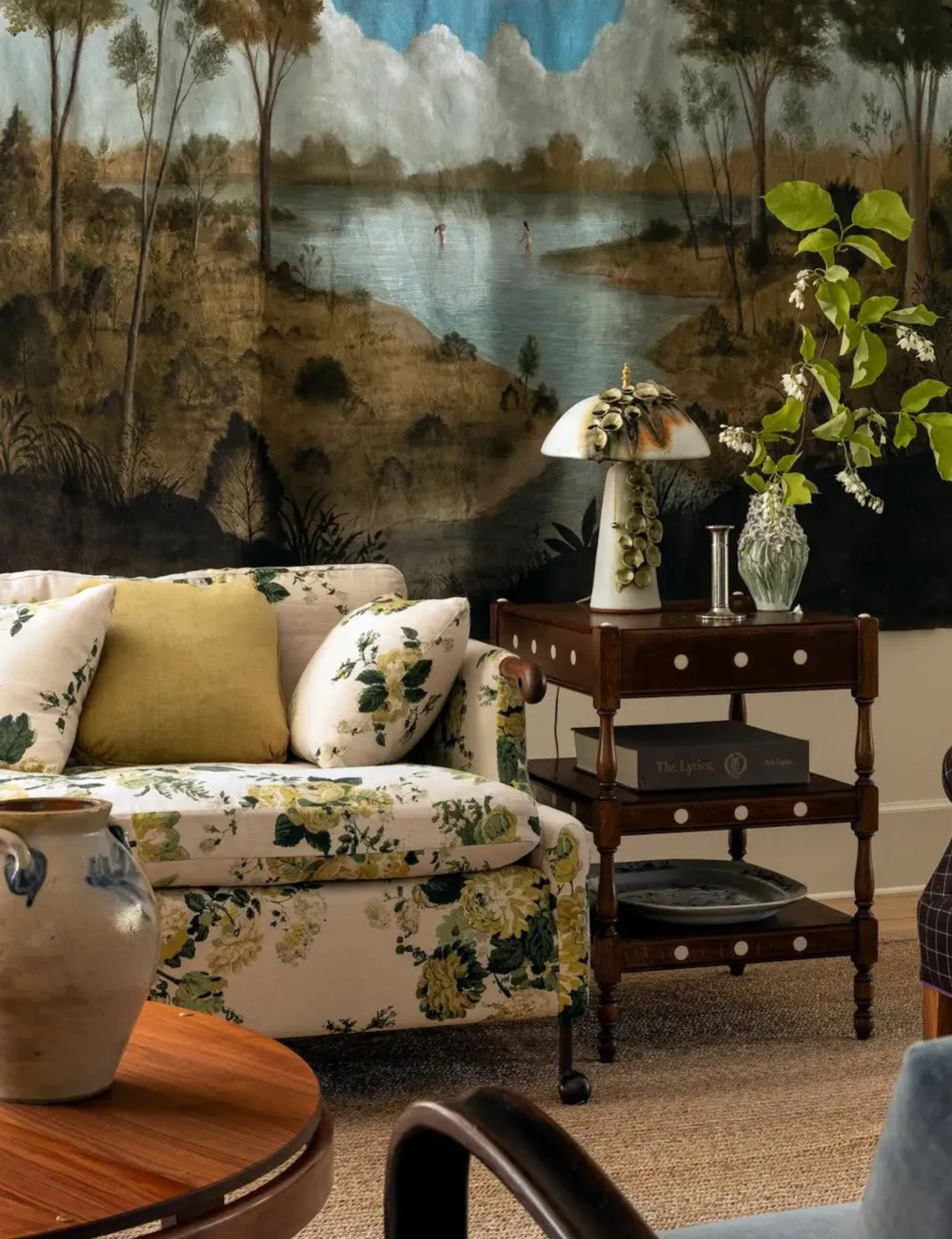 old meets new cozy living room with a large wall hung tapestry, a neutral and yellow floral sofa with antique wooden furniture and ceramics