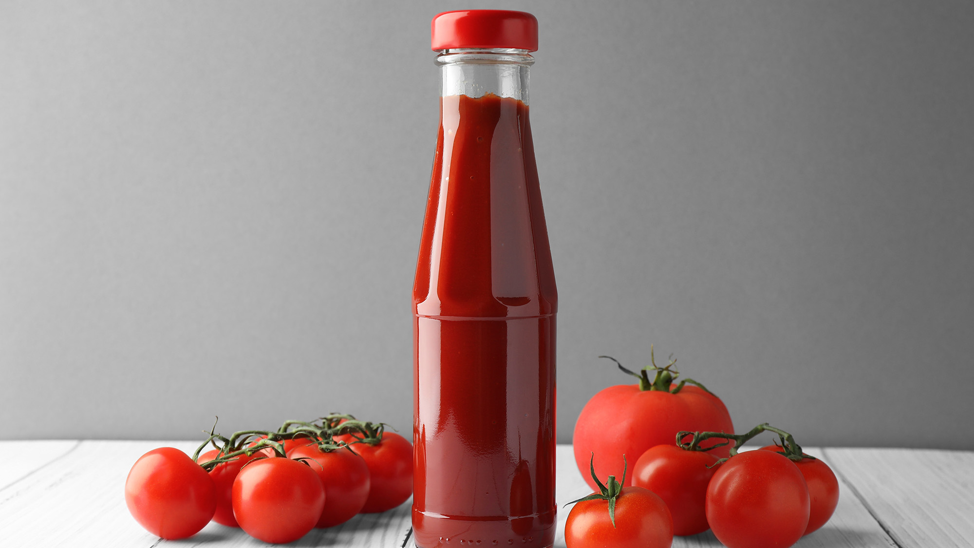 Bottle of ketchup surrounded by fresh tomatoes