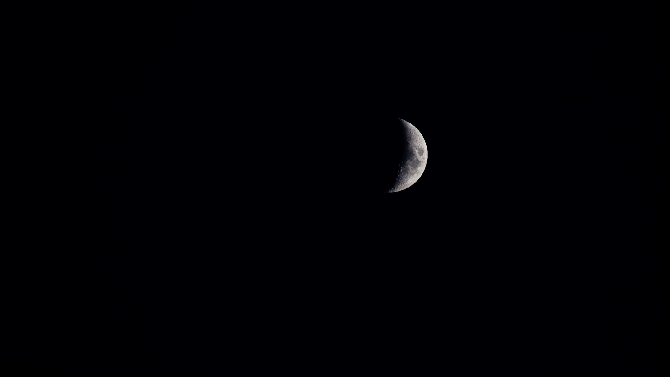 A small crescent moon in the night sky with some lunar seas and craters visible.