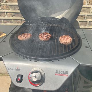 a close up of a barbecue grill with three burgers cooking on top