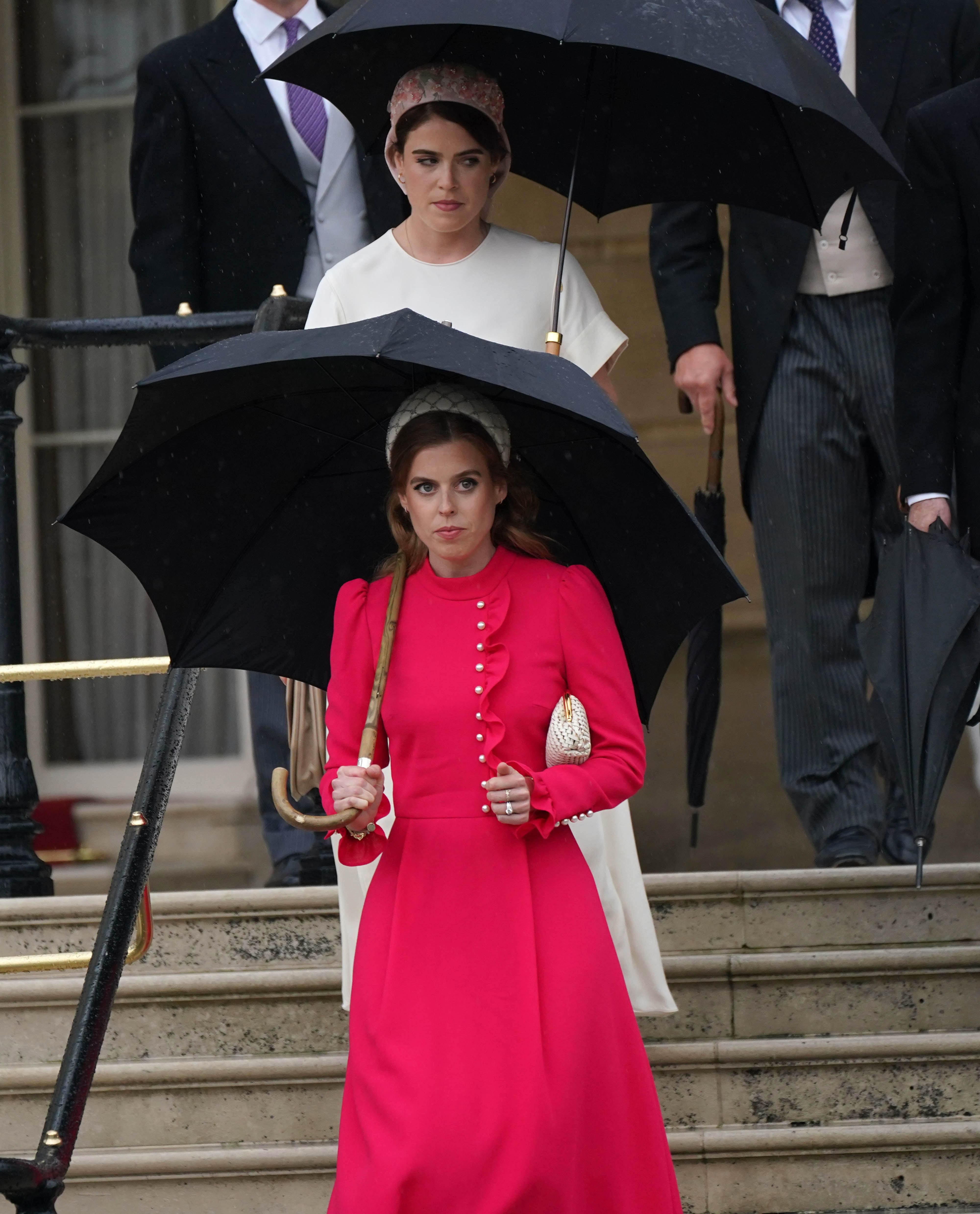 Princess Beatrice and Princess Eugenie holding black umbrellas walking down stairs