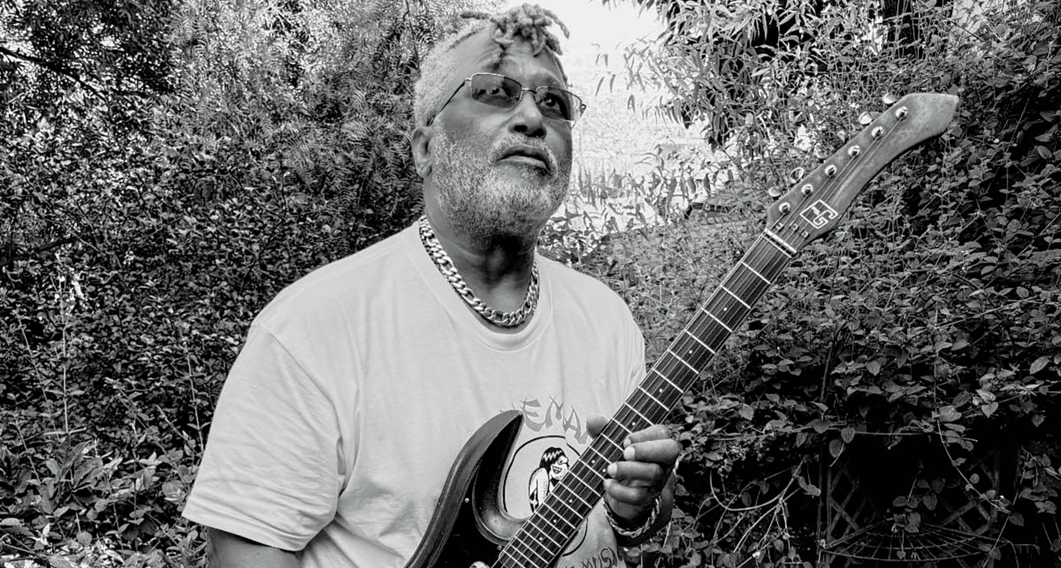 A black-and-white photo of P-Funk legend Michael Hampton with his Guyatone, in amongst heavy foliage.