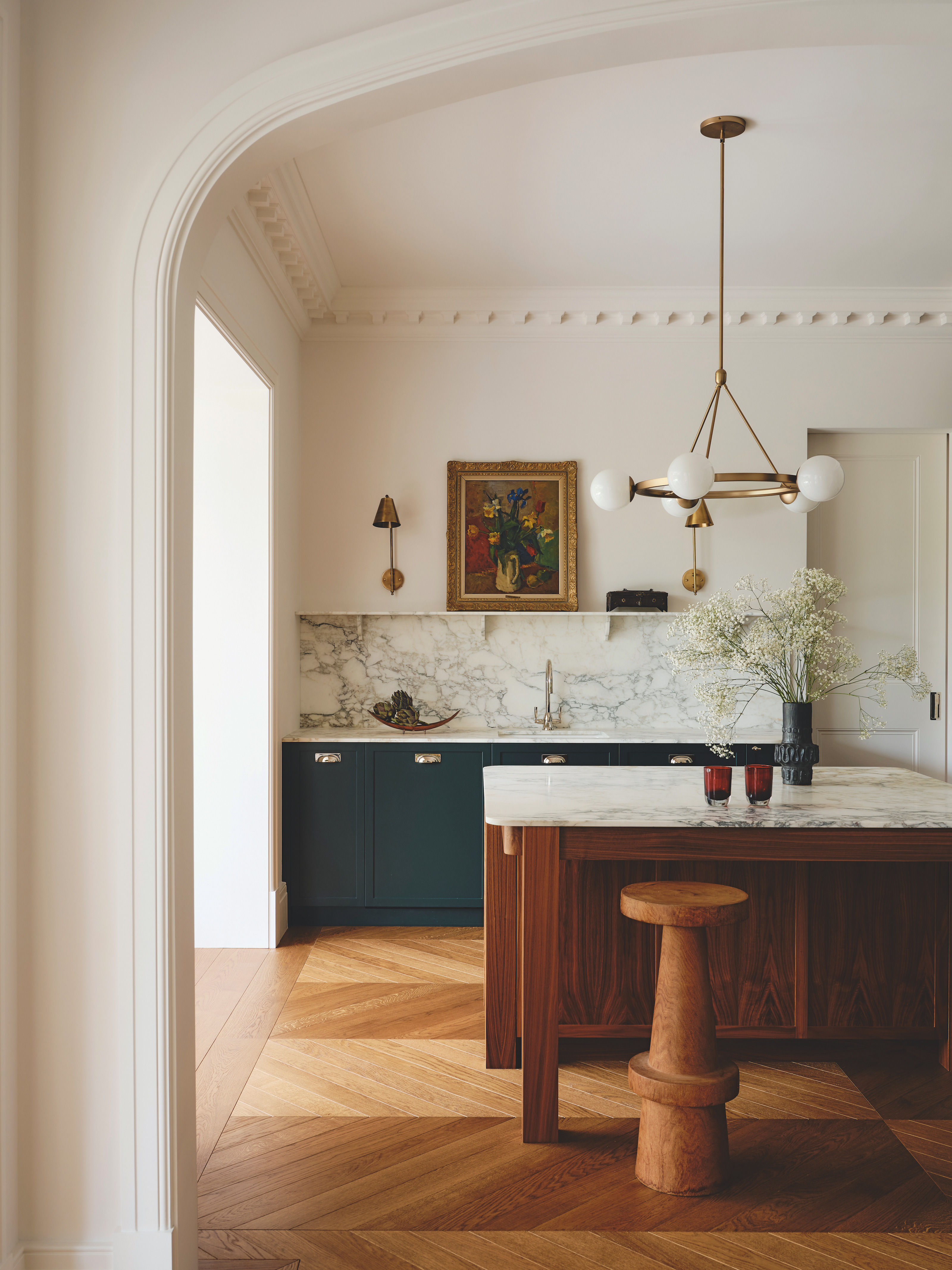 A modern kitchen with traditional features, a wooden island with white marble and navy cupboards, with a modern chandelier above.