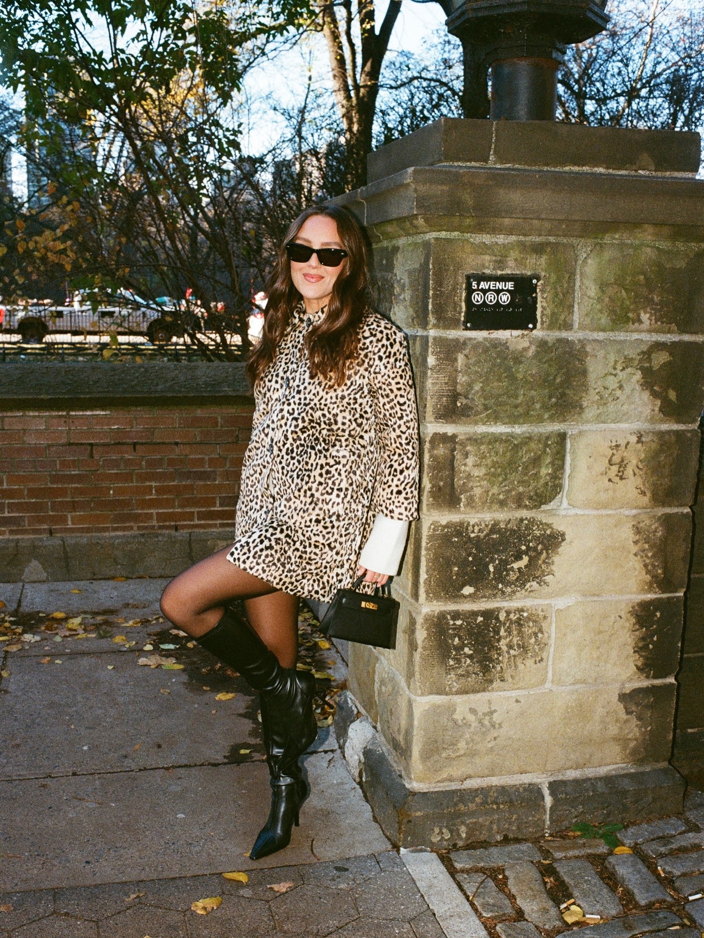 An image of @emmaleger wearing a leopard-print coat with a mini Hermes Kelly and heeled knee-high boots.
