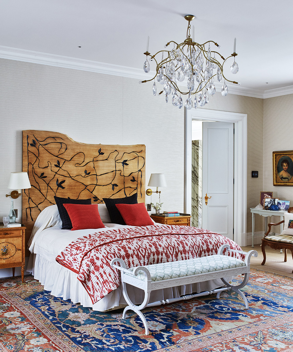 An example of bedroom ceiling light ideas showing a wooden bed with a decorative headboard with red and black cushions below a large chandelier