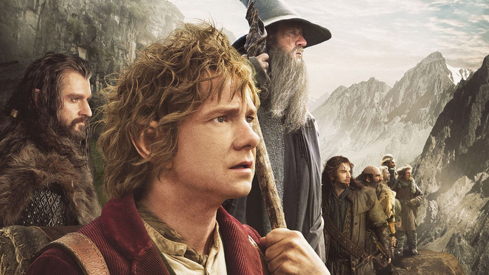 A promo shot for The Hobbit showing the main characters, including Bilbo Baggins and Gandalf, looking off into the distance surrounded by mountains.