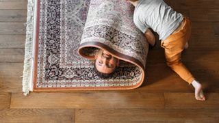 Image of man being rolled up in carpet by son