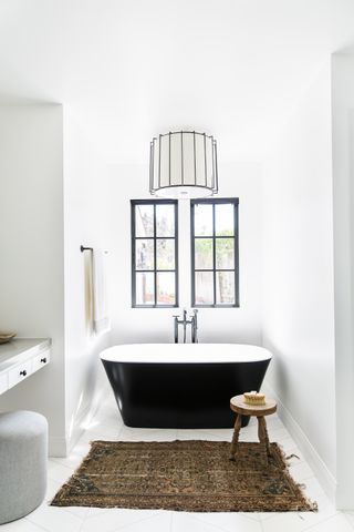 monochromatic bathroom with vintage rug and rustic stool, black framed window and tub