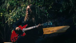 Sammy Boller is photographed in front of some foliage with a red Gibson ES-335.