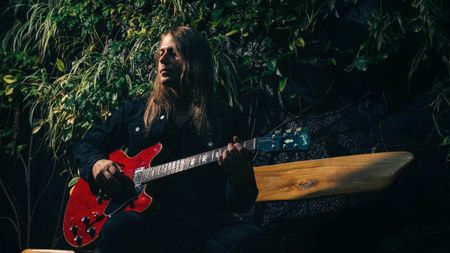 Sammy Boller is photographed in front of some foliage with a red Gibson ES-335.