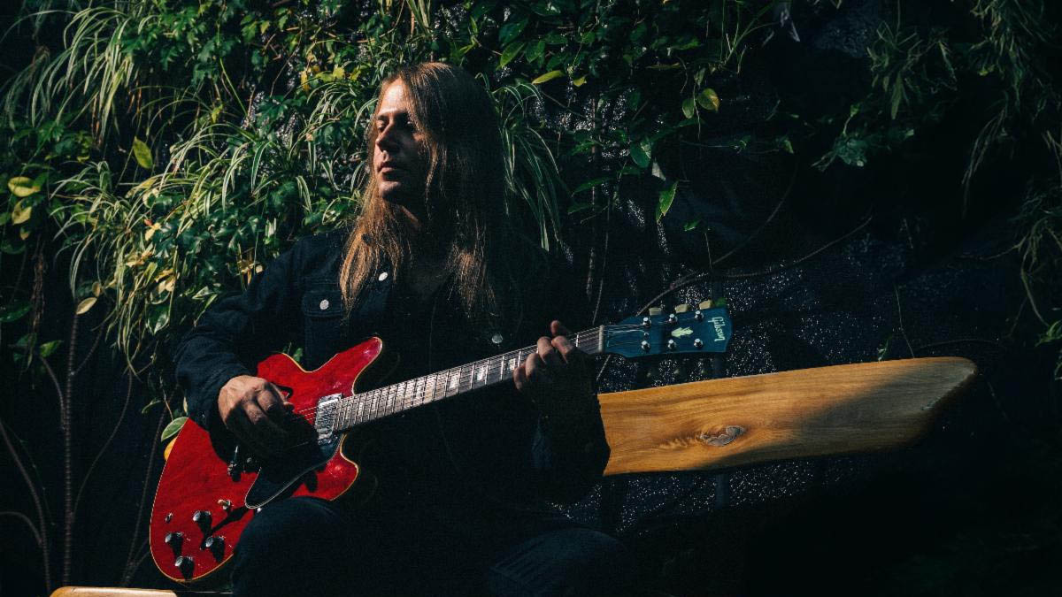 Sammy Boller is photographed in front of some foliage with a red Gibson ES-335.