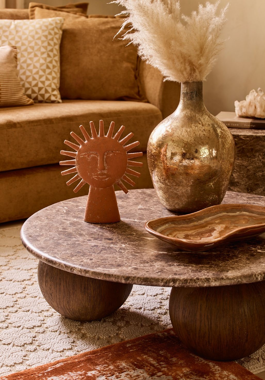 Orange sofa with cream rug, travertine top coffee table with round lets and a vase and ornaments on top.