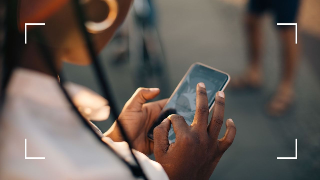 View of woman from over her shoulder, wearing gold earrings, looking at phone and learning how to sext