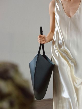 A model in cream silk dress, holding a black hobo style open bag with thin straps