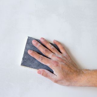 hand sanding a white wall with sandpaper