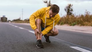 Runner in yellow jacket crouches down and holds his shin
