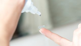 How to clean contact lenses: A person uses solution to clean a contact lens balanced on their finger