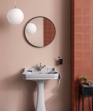 Terracotta bathroom with pedestal sink and round mirror