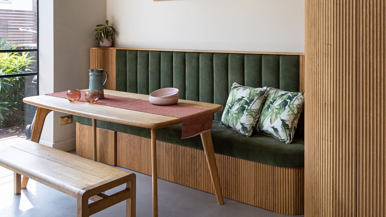 Kitchen with breakfast nook in wood panelling with green cushions.