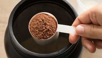 A hand scooping protein powder out a tub