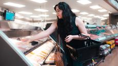 Woman reaches for packet from open refrigerated shelving in a grocery store
