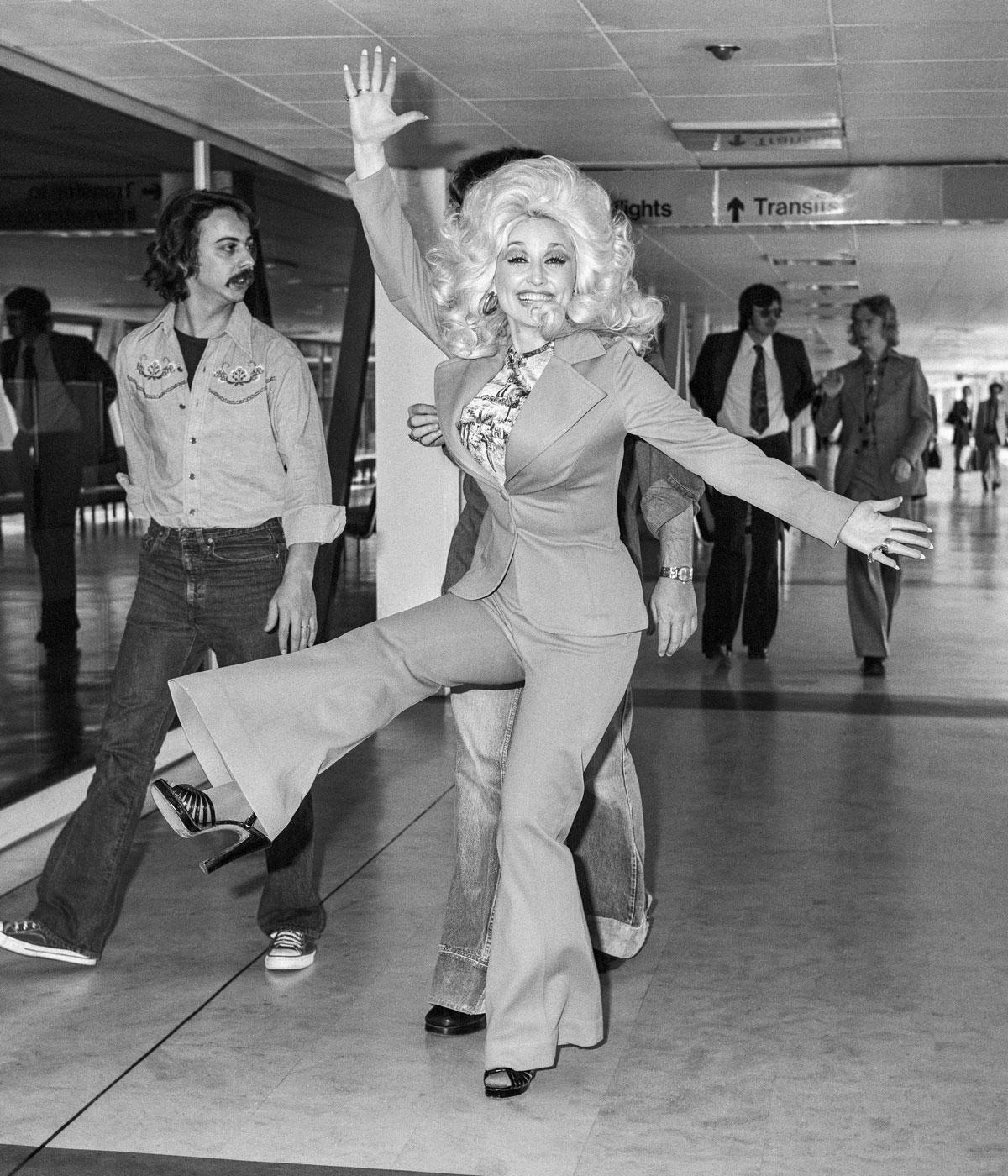 Black and white image of Dolly Parton in a suit doing a kick