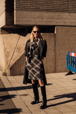 Poppy Delevingne in a black plaid dress, black boots, and trench coat at London fashion week