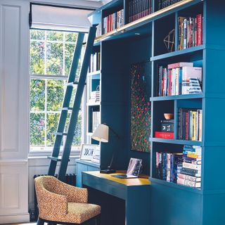 Home office with built-in blue wall storage unit with ladder.