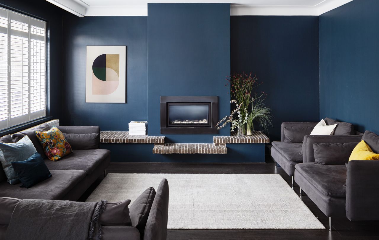 A living room with dark blue walls and dark gray sofas