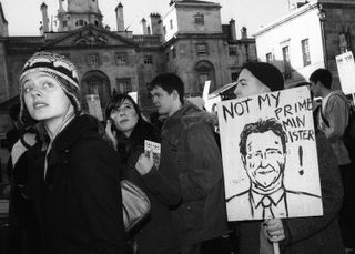 A black & white photo of people protesting. There is a sign that says 'Not my prime minister'.