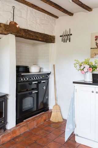 terracotta tiles in a white cottage kitchen with black range cooker in fireplace
