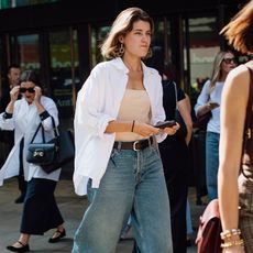 Woman is walking wearing jeans, tube top, and open white button down shirt