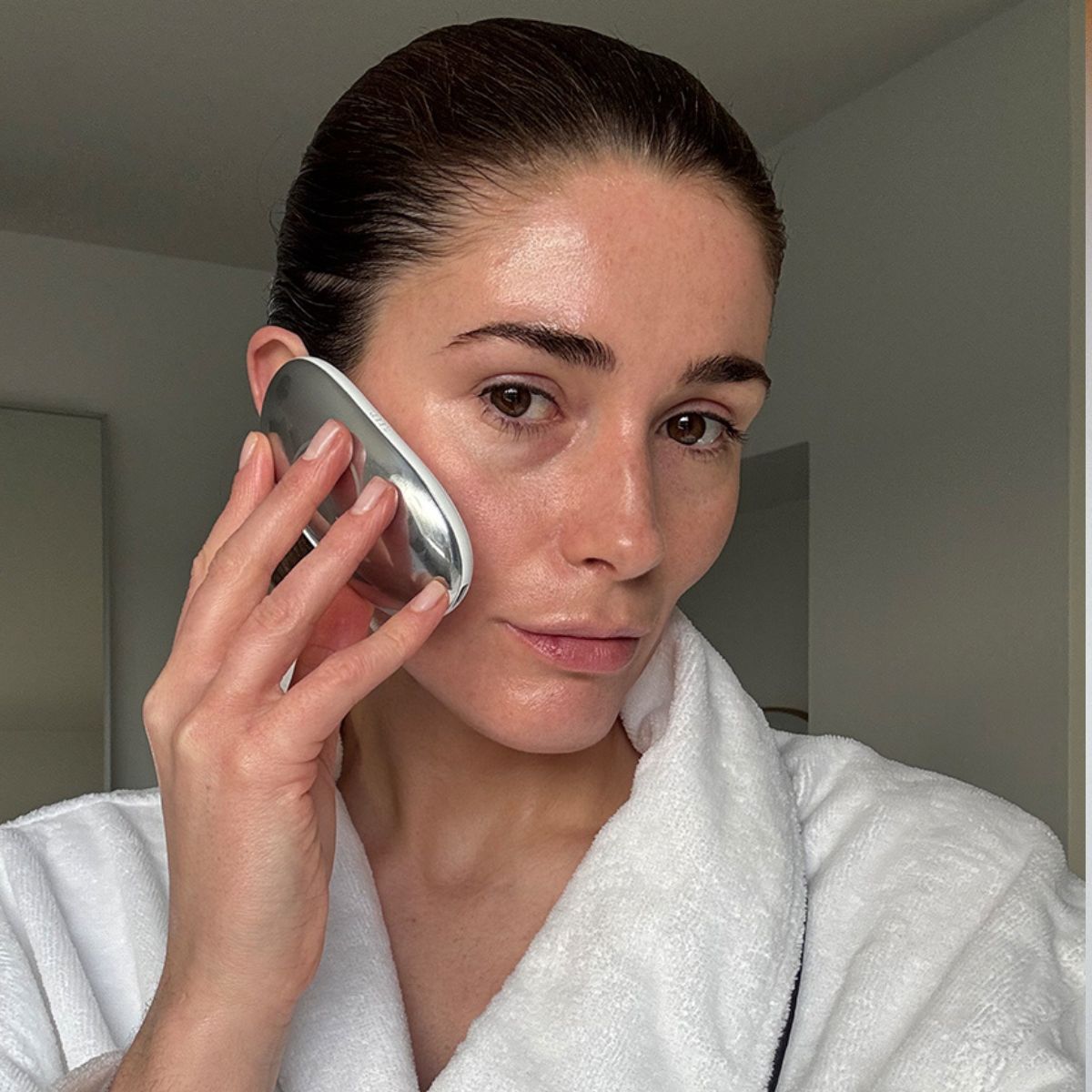 A selfie of Eleanor using the Ziip Halo device on her cheek while wearing a white dressing gown