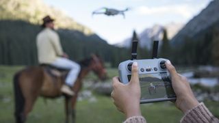 DJI R2 remote controller in pilot's hands, with subject and DJI Mini 4 Pro drone and mountain backdrop