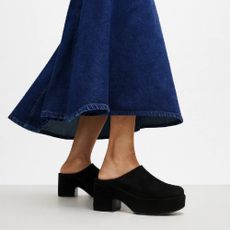 A model from the waist down wearing a long denim skirt and a pair of black heeled clogs from FitFlop.