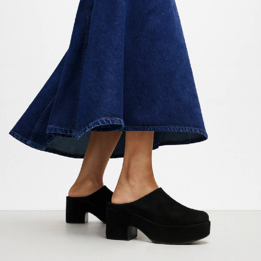 A model from the waist down wearing a long denim skirt and a pair of black heeled clogs from FitFlop.