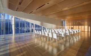 An auditorium featuring wooden floors and ceilings with clear glass panels . The room has white chairs set in a conference seating style